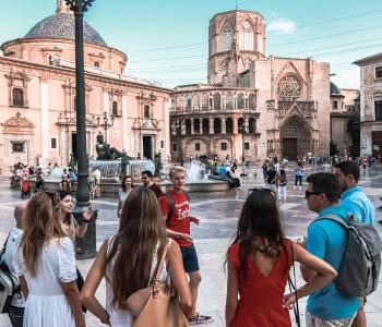 Grupo de personas jóvenes en una plaza, escuchando a su guía turístico