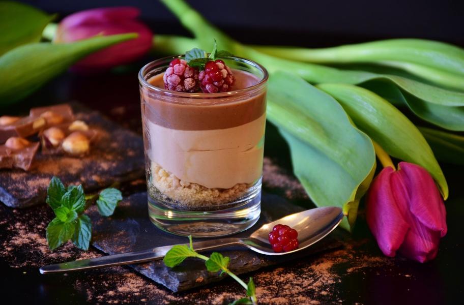 vaso de chocolate con frutos del bosque sobre mesa decorada con flores y chocolate